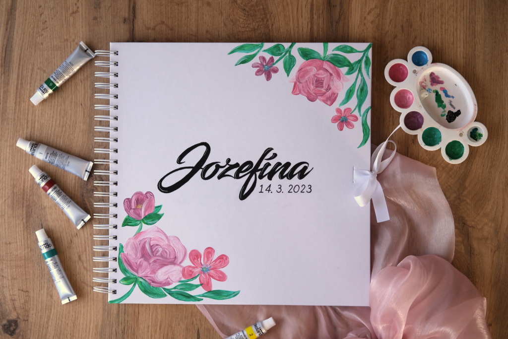 Biela fotokniha s kvetmi, ručne maľovaný album s nápisom Jozefína, ružové kvety a zelené listy.